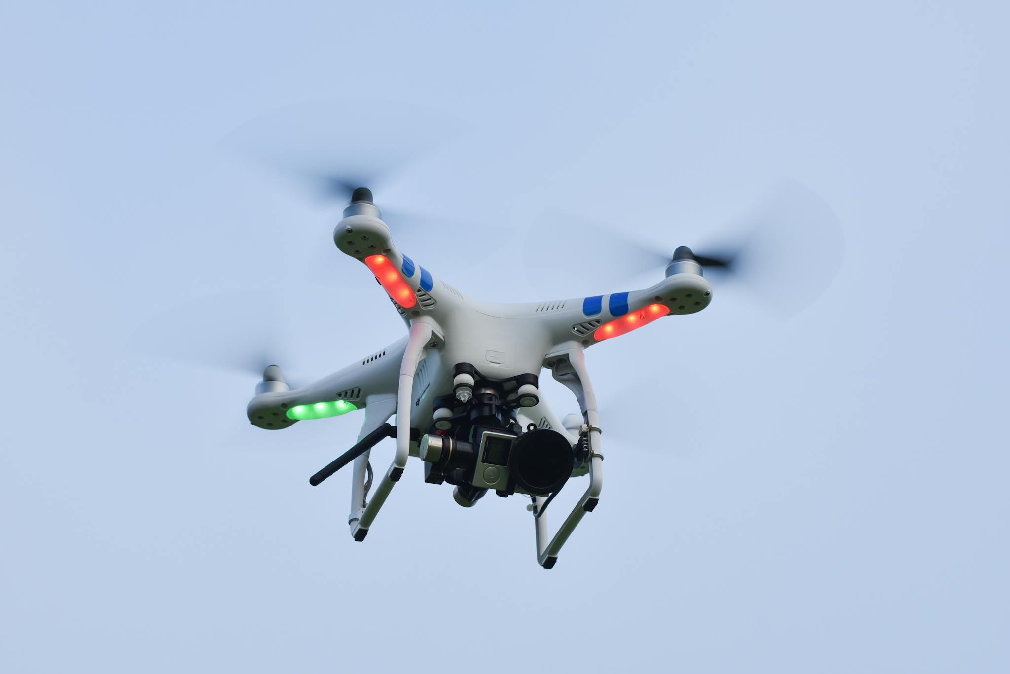 Close-up of a quadcopter drone flying with camera against a clear blue sky.